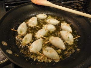 Stuffed calamari frying in olive oil on the stove.