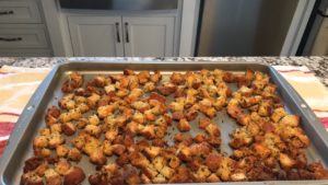 Croutons spread out on a baking sheet, coated in olive oil, garlic and herbs and ready to go into the oven.